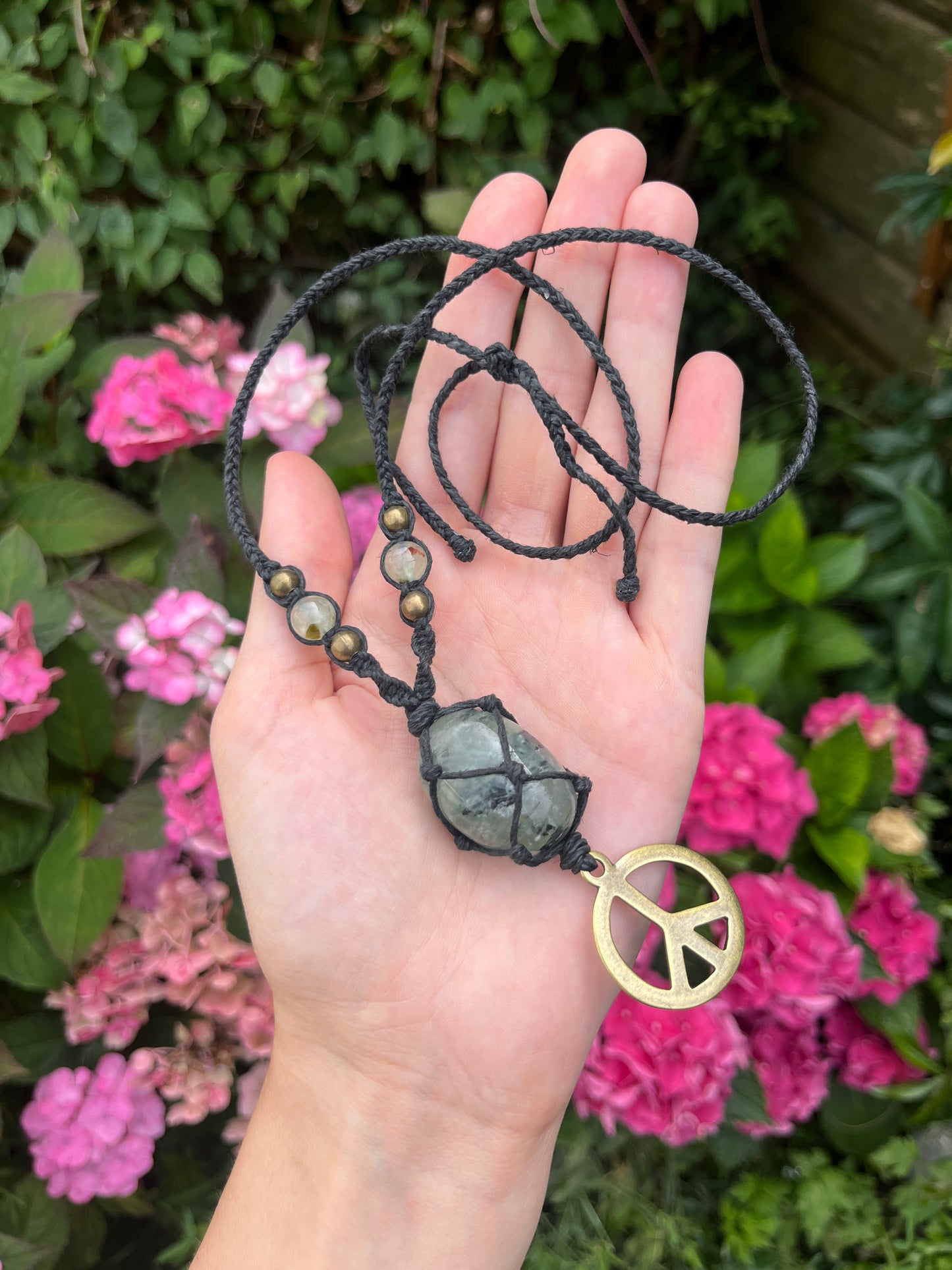 Hand holding a necklace with a peace sign pendant against a floral background