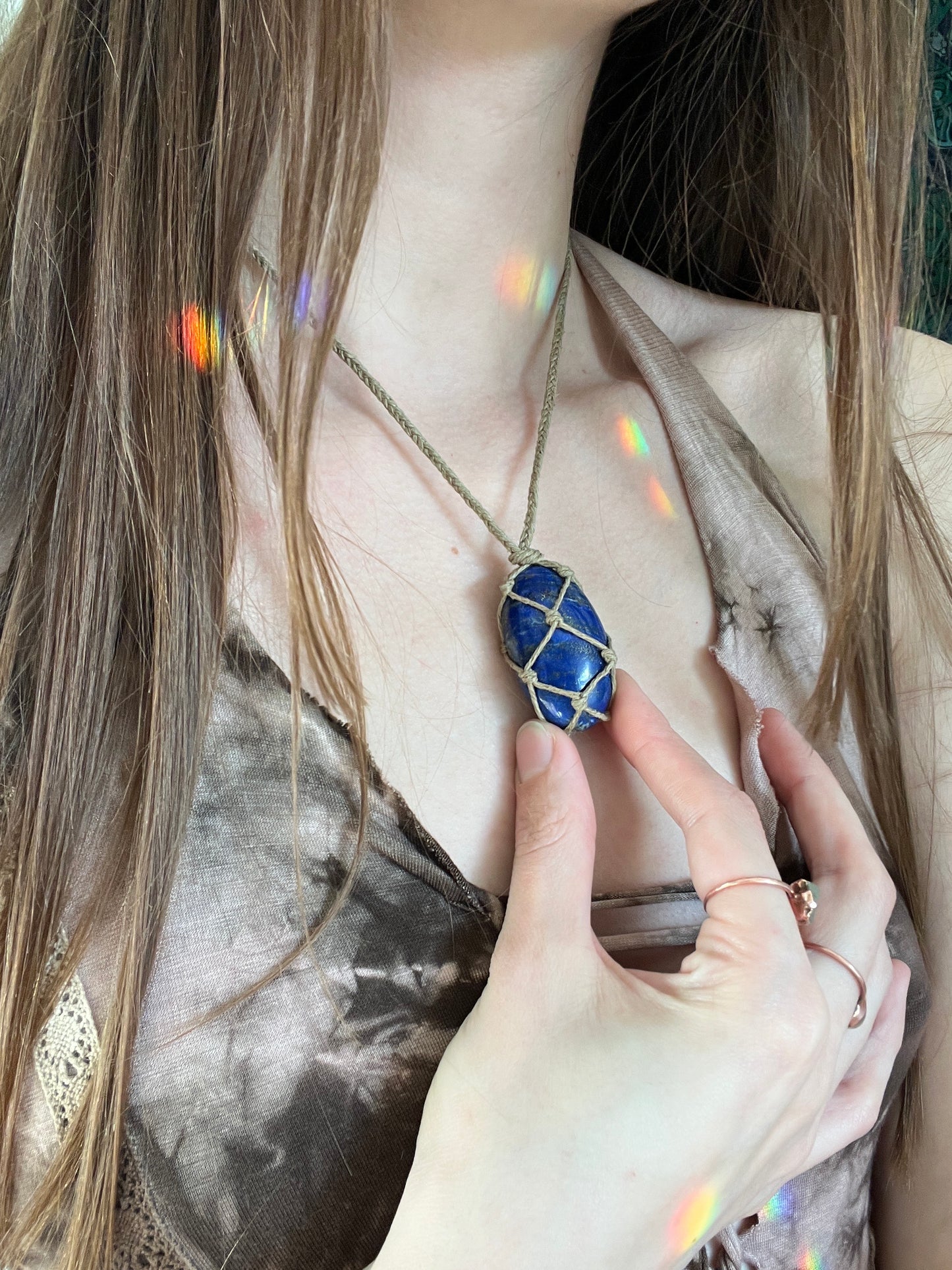 Handmade macrame necklace with an Lapis Lazuli crystal wrapped in hemp cord, featuring gemstone beads and spiral metal accents. Bohemian jewellery displayed on green moss with a rustic wood background